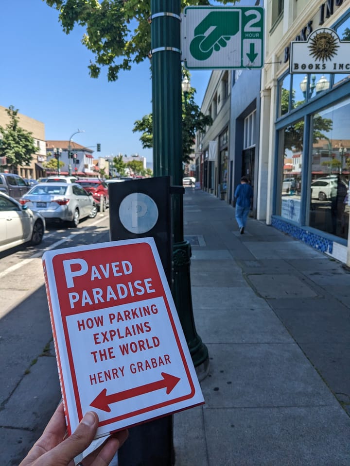 picture of a book titled "Paved Paradise: How Parking Explains the World" by Hengry Grabar held aloft in downtown Alameda